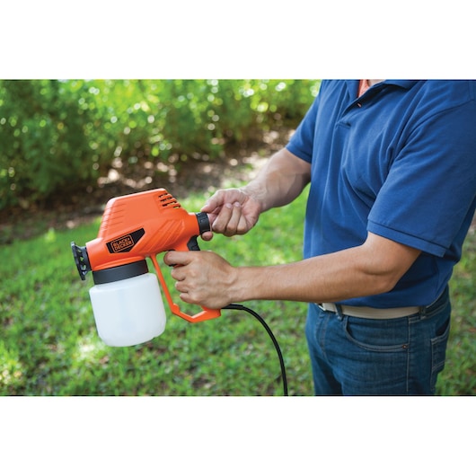 Person holding BLACKDECKER BDPS130 orange electric paint sprayer outdoors.