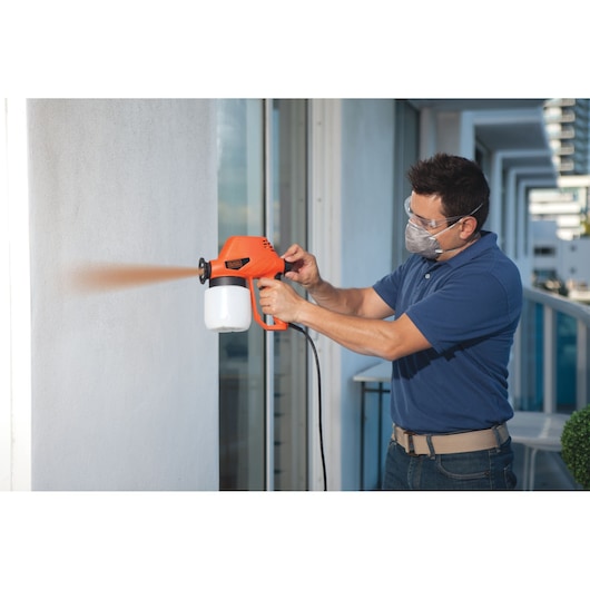 Person using BLACKDECKER BDPS130 paint sprayer to apply paint on exterior wall.