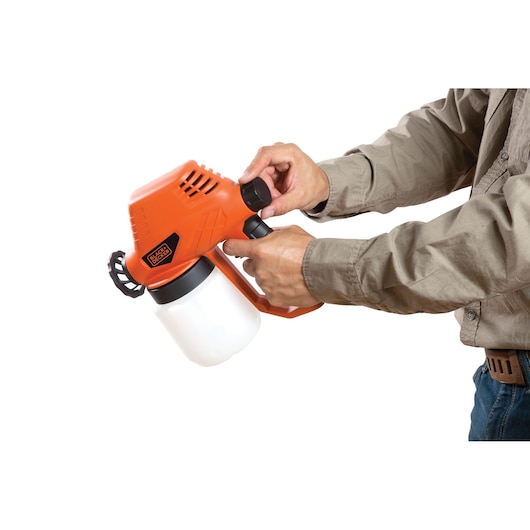Photo of BLACKDECKER BDPS130 handheld paint sprayer, orange and black, held by a person adjusting the nozzle.