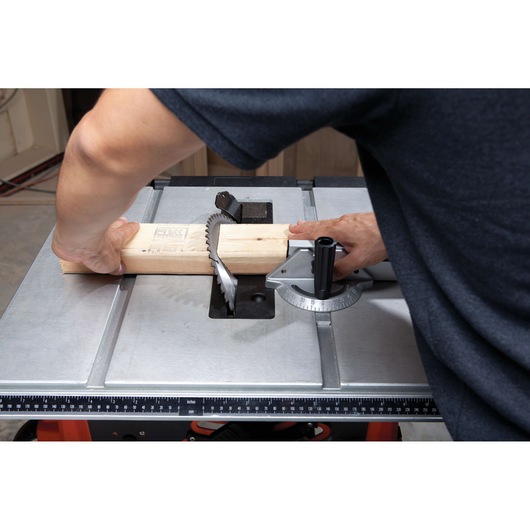 Photo of BLACKDECKER BDTS1800 table saw cutting a wooden board, close-up angle with user's hands guiding the wood.