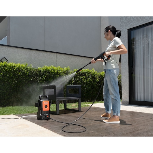 BLACK+DECKER BEPW1300 pressure washer in use cleaning outdoor furniture on patio.