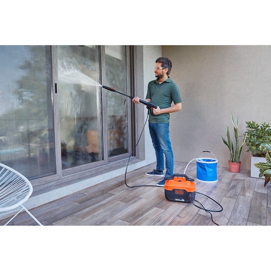 BLACKDECKER BEPW1600H pressure washer used outdoors to clean glass sliding doors, with plants nearby.