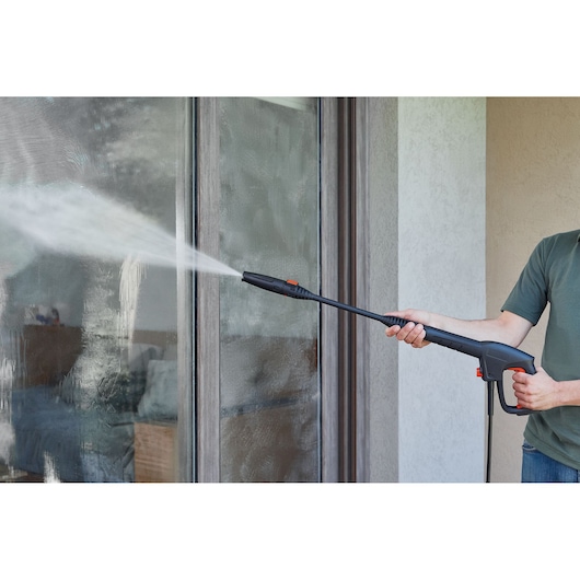 BLACKDECKER BEPW1600H pressure washer spraying water to clean large glass window outdoors.