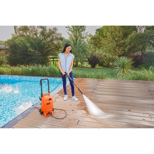 BLACKDECKER BEPW1800T pressure washer cleaning wood deck near pool outdoors.