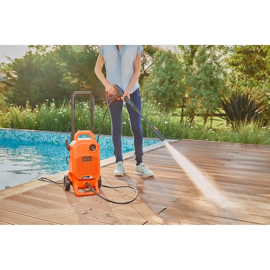 BLACKDECKER BEPW1800T pressure washer being used to clean a wooden deck near a pool.