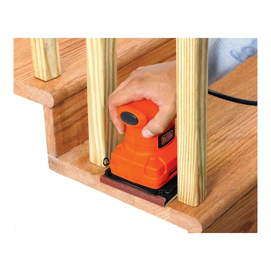 BLACKDECKER BS200 palm sander used on wooden stairs, close-up view showing orange tool and sanding work.
