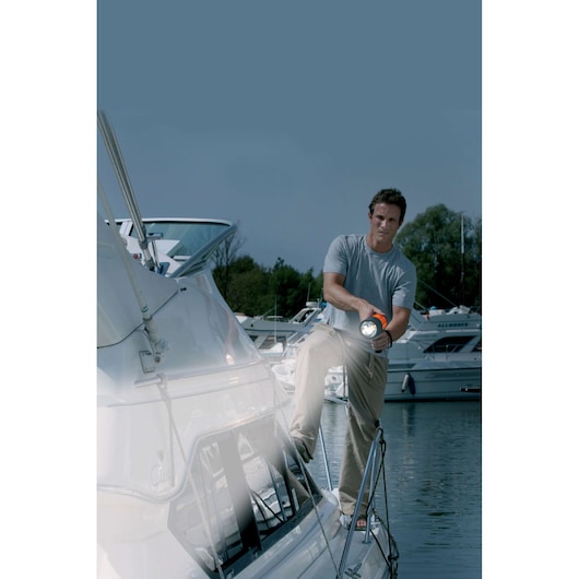 BLACKDECKER BSL100 flashlight in use on a boat, person shining light on deck, marina background.