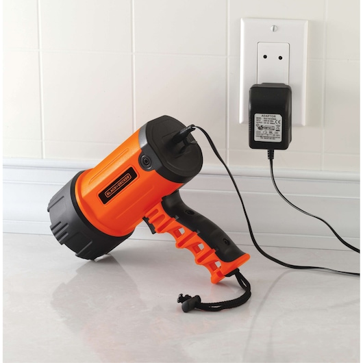 BLACKDECKER BSL100 orange and black handheld spotlight charging with wall adapter, side view on white counter.