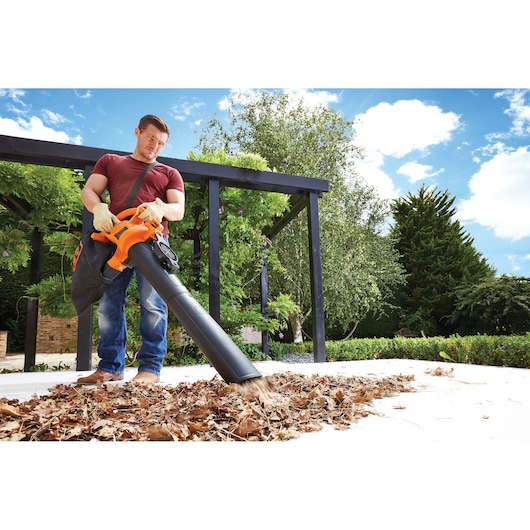 BLACKDECKER BV25 leaf blower in use outdoors, blowing dry leaves on a patio.