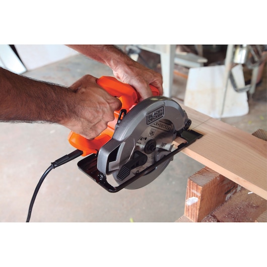 BLACKDECKER CS1004 orange and gray circular saw cutting wood, shown in workshop setting.