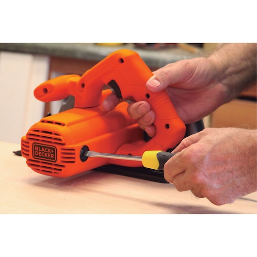 BLACKDECKER CS1004 orange hand sander being adjusted with a screwdriver on a workbench.