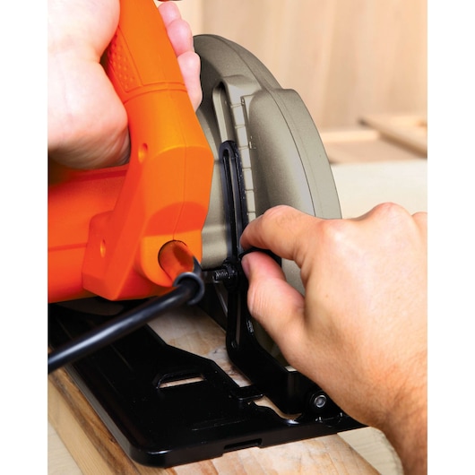 Photo of hands adjusting BLACKDECKER CS1024 circular saw, close-up view of orange handle and blade guard.