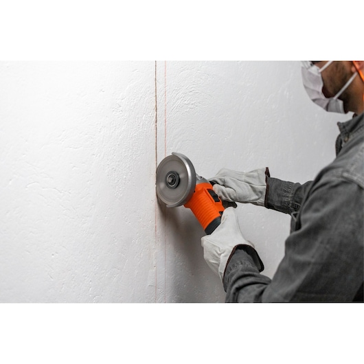 BLACKDECKER G720X angle grinder with orange casing used to cut a line on a white wall.