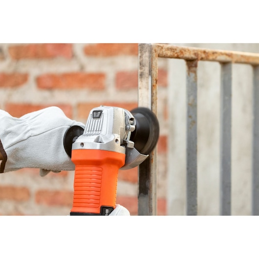 BLACKDECKER G720X angle grinder in use on a metal fence, orange and silver body held by a gloved hand.