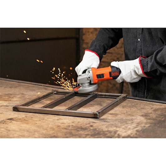 Photo of BLACK+DECKER G720X angle grinder producing sparks while grinding metal frame, user wearing gloves.