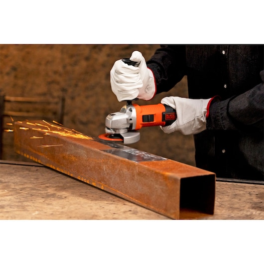 BLACKDECKER G720X angle grinder in use, sparks flying from grinding rusty steel pipe.