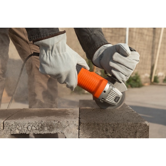 BLACKDECKER G720X angle grinder in use, cutting concrete block outdoors, operator wearing protective gloves.