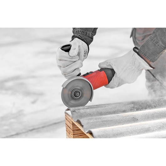 Photo of BLACKDECKER G720X angle grinder in use cutting a corrugated sheet, worker wearing gloves.