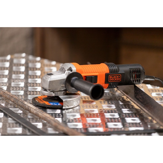 A BLACK+DECKER angle grinder with an orange and black handle, shown placed on a metal surface.