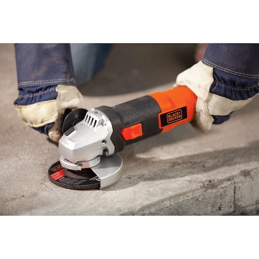 Photo of BLACKDECKER G720 angle grinder in use on concrete, orange and black body, gloved hands holding tool.