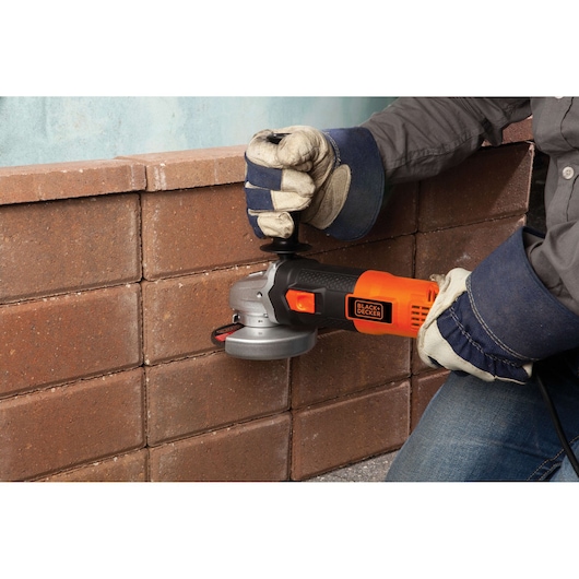 Photo of BLACKDECKER G720 angle grinder used on brick wall, orange and black tool held with gloves.