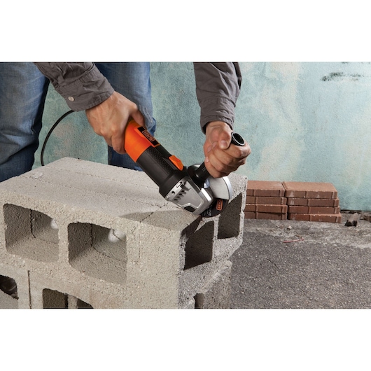 BLACKDECKER G720 angle grinder cutting concrete block, close-up outdoor scene.