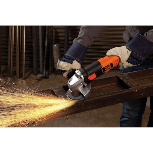BLACKDECKER G720 angle grinder in use grinding metal, orange and black handle, worker wearing gloves.