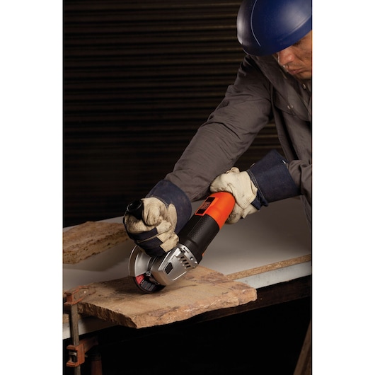 BLACKDECKER G720 angle grinder in use cutting stone, worker wearing gloves and safety gear.