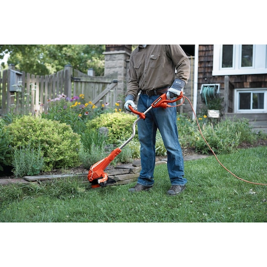 Person using BLACKDECKER GH750 electric string trimmer to edge a lawn along garden border.