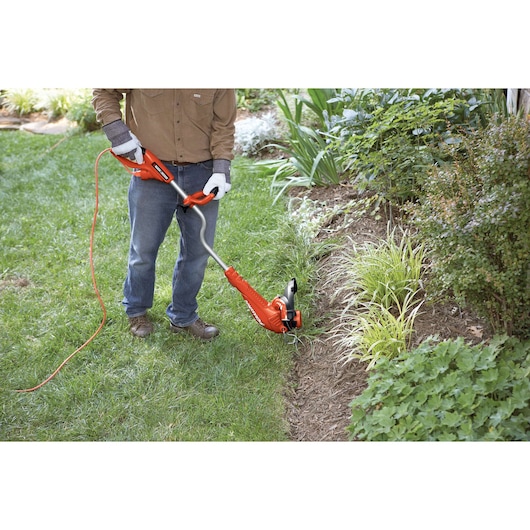 Photo of a person using a BLACKDECKER GH750 electric string trimmer to edge a garden lawn.