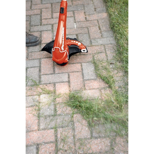 BLACKDECKER GH750 orange string trimmer in use on brick walkway with scattered grass clippings.