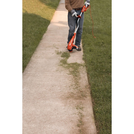 BLACKDECKER GH750 string trimmer edging grass along a sidewalk, person holding orange electric tool.