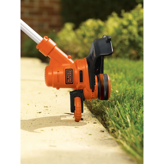Photo of BLACK+DECKER GH900 string trimmer edging a lawn along a sidewalk, showing the orange tool in use.