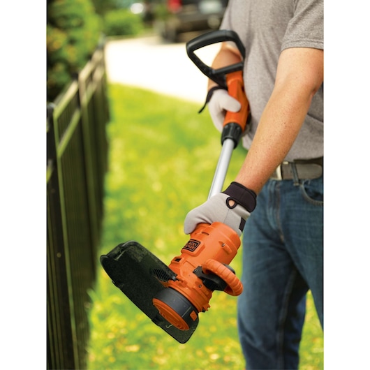 Photo of BLACKDECKER GH900 string trimmer in use, orange and black, held by person wearing gloves outdoors.