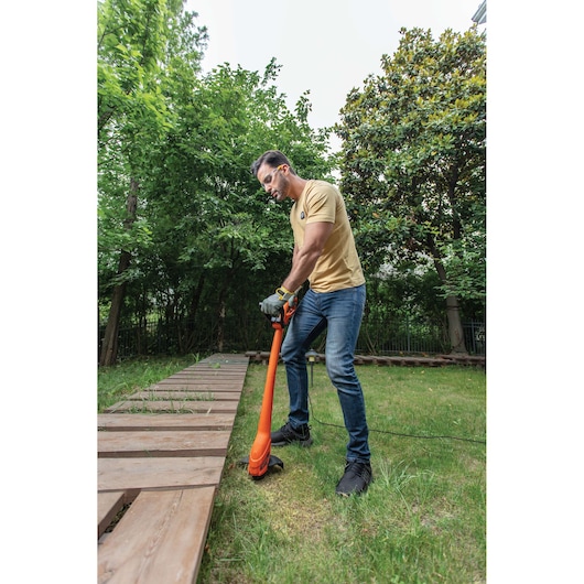 Photo of person using BLACKDECKER GL350 orange grass trimmer on garden lawn near wooden path.