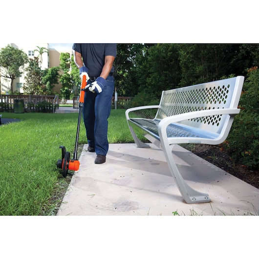BLACKDECKER GL600N electric grass trimmer in use, shown edging lawn along sidewalk in outdoor setting.
