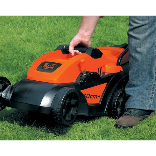 Photo of BLACK+DECKER GR3000 lawn mower in use on green grass, close-up of orange and black mower with handle and wheels.
