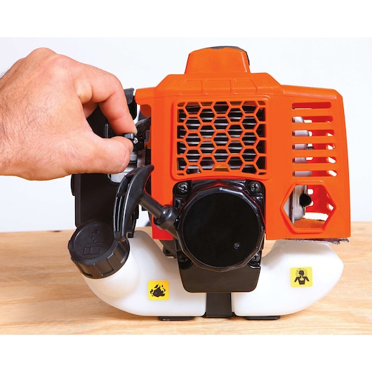 BLACKDECKER GST33 grass trimmer engine close-up with hand adjusting choke lever, orange housing, side angle.