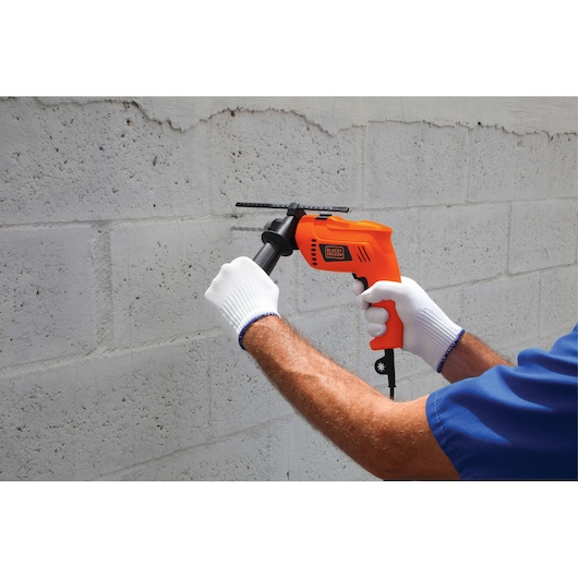 Photo of BLACK+DECKER HD555 electric drill in use on a concrete wall, handled by a person wearing white gloves.