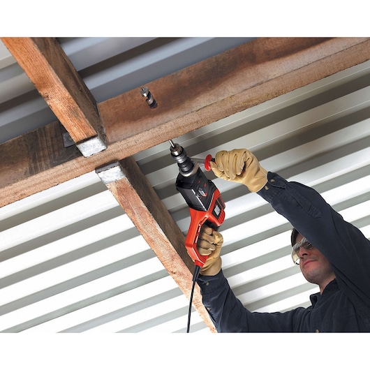 Person using BLACKDECKER KD975KA corded drill to drill into wood beam overhead, wearing gloves.