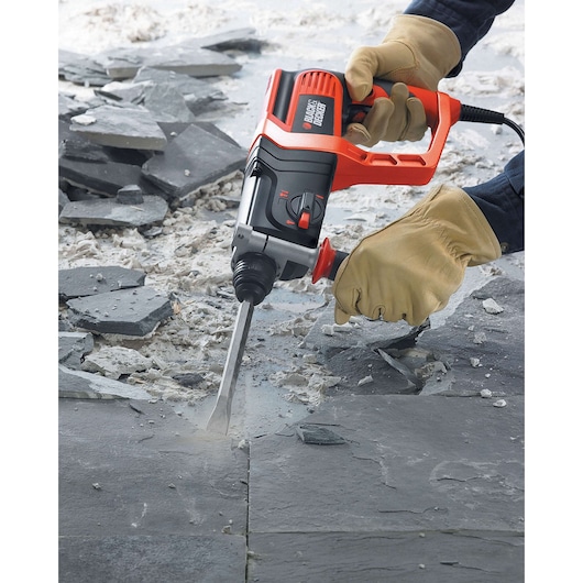 BLACKDECKER KD975KA rotary hammer drill in use with chisel bit breaking stone tiles, worker wearing gloves.