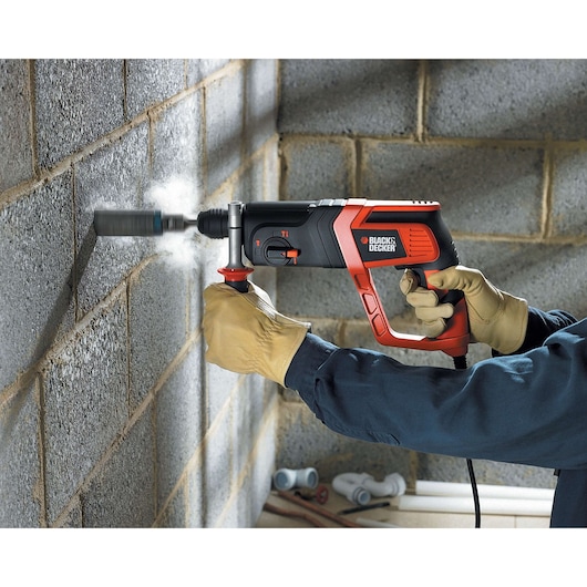 Photo of BLACK+DECKER KD975KA hammer drill in use, drilling into a concrete wall, close-up side view.