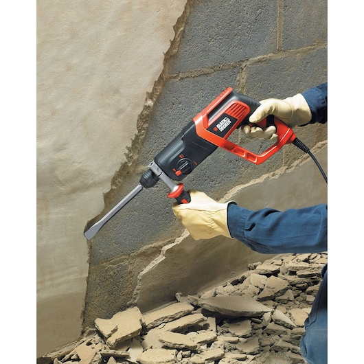 BLACKDECKER KD975KA rotary hammer drill used for chipping concrete, side view, construction gloves visible.