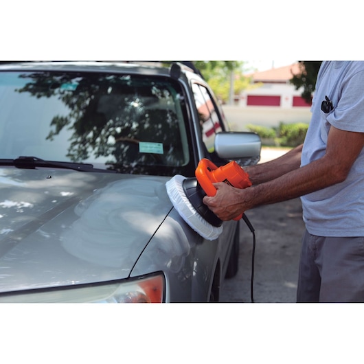 Photo of a person using BLACKDECKER KP12K car polisher on a gray car hood outdoors.