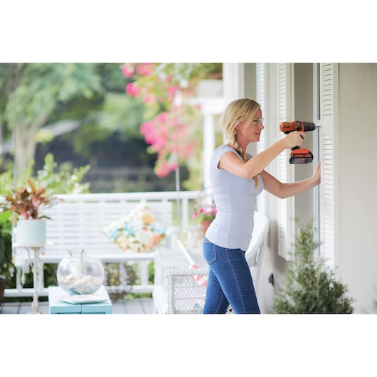 Photo of a woman using a BLACKDECKER LD120 cordless drill outdoors, drilling into white shutters.