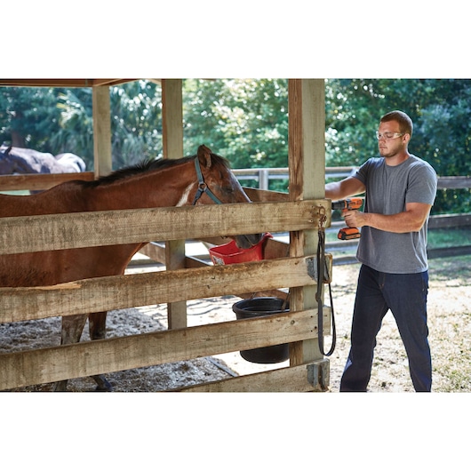 Photo of a person using a BLACKDECKER LD120 cordless drill on a wooden fence near a horse in a barn setting.