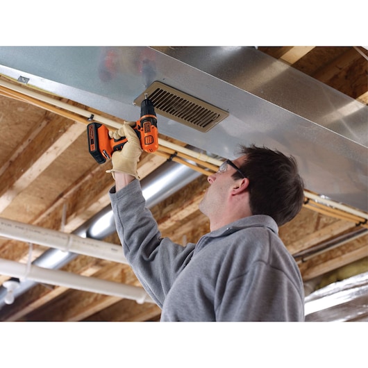 Photo of a person using BLACK+DECKER LD120 cordless drill on a metal vent in a basement ceiling.