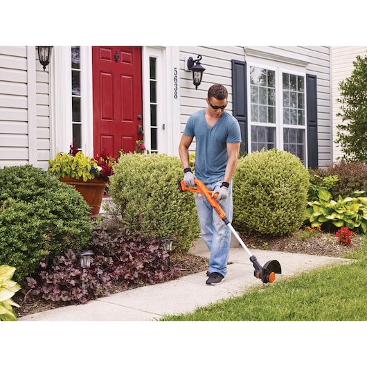 BLACKDECKER LST201 orange cordless string trimmer used to edge grass along a walkway in front of a house.