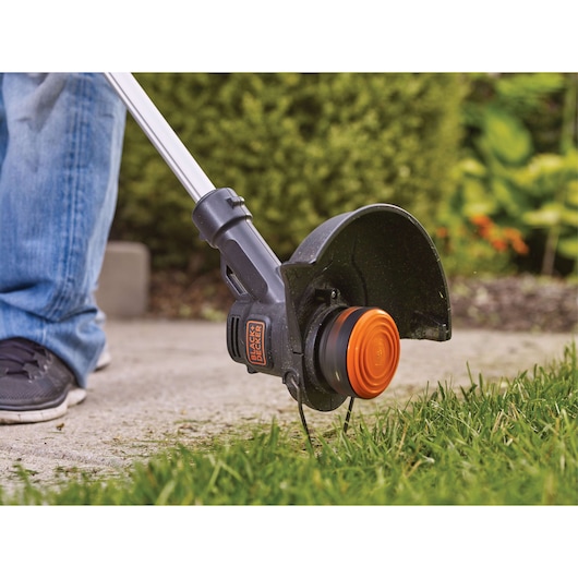 Photo of BLACKDECKER LST201 string trimmer in use edging grass along a concrete walkway outdoors.