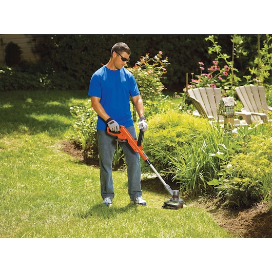 Person using BLACK+DECKER LST300 orange string trimmer in a garden to edge along flower beds.